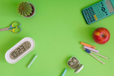 Yeşil bir arkaplanda düzenli olarak dizilmiş not defterleri, kalemler, keçeli kalemler ve makaslar da dahil olmak üzere okul malzemelerinden oluşan canlı bir çeşitlilik.