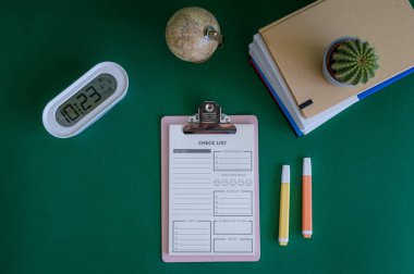 Yeşil bir arkaplanda düzenli olarak dizilmiş not defterleri, kalemler, keçeli kalemler ve makaslar da dahil olmak üzere okul malzemelerinden oluşan canlı bir çeşitlilik.