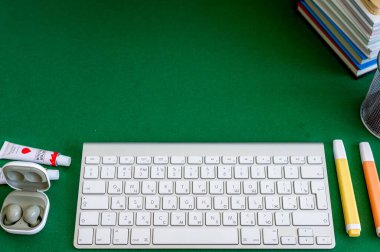 Yeşil bir arkaplanda düzenli olarak dizilmiş not defterleri, kalemler, keçeli kalemler ve makaslar da dahil olmak üzere okul malzemelerinden oluşan canlı bir çeşitlilik.