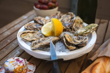 Limon, kabuklu baget, kremalı tereyağı ve bir bardak geleneksel Fransız şarabı ile servis edilen lezzetli çiğ istiridye tabağı..