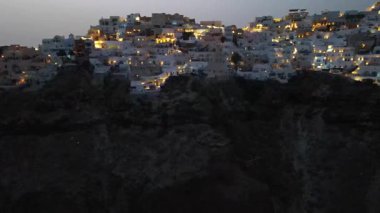 Günbatımında Yunanistan 'ın Santorini adasındaki Oia köyünün çarpıcı hava manzarası. İkonik beyaz yıkanmış evler, mavi kubbeler ve altın ışık nefes kesici ve romantik bir atmosfer yaratır..