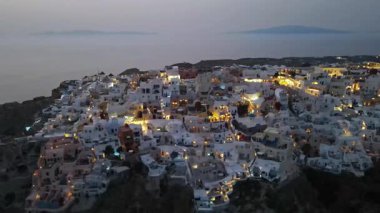 Günbatımında Yunanistan 'ın Santorini adasındaki Oia köyünün çarpıcı hava manzarası. İkonik beyaz yıkanmış evler, mavi kubbeler ve altın ışık nefes kesici ve romantik bir atmosfer yaratır..