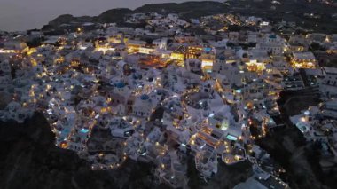 Günbatımında Yunanistan 'ın Santorini adasındaki Oia köyünün çarpıcı hava manzarası. İkonik beyaz yıkanmış evler, mavi kubbeler ve altın ışık nefes kesici ve romantik bir atmosfer yaratır..