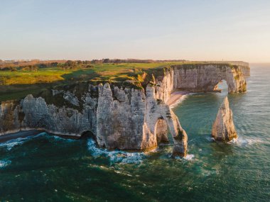 Etretat 'ın ikonik tebeşir kayalıkları ve turkuaz suları güneş ışığı altında parlayarak Normandiya' nın doğal güzelliğini ve huzurlu sahil şeridini gözler önüne seriyor..