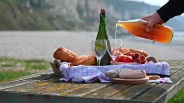 Normandiya 'da Fransız cilası, bölgesel peynir ve taze elmaların yer aldığı samimi bir plaj pikniği manzaralı bir sahilin arka planında geçiyor.
