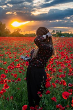 Güzel bir kız canlı kırmızı gelinciklerin arasında duruyor, gülümsüyor ve yaz melteminin tadını çıkarıyor. Sahne mutluluğu, rahatlığı ve doğanın güzelliğini tam çiçeklenirken yakalar..