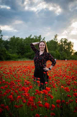 Güzel bir kız canlı kırmızı gelinciklerin arasında duruyor, gülümsüyor ve yaz melteminin tadını çıkarıyor. Sahne mutluluğu, rahatlığı ve doğanın güzelliğini tam çiçeklenirken yakalar..