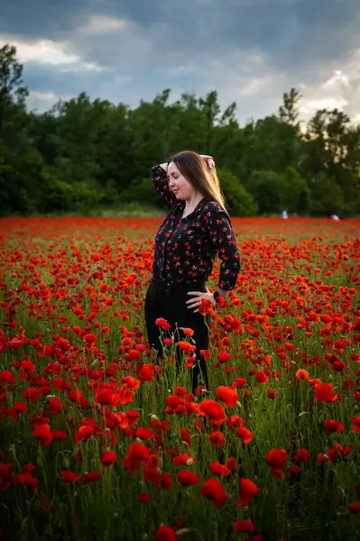 Güzel bir kız canlı kırmızı gelinciklerin arasında duruyor, gülümsüyor ve yaz melteminin tadını çıkarıyor. Sahne mutluluğu, rahatlığı ve doğanın güzelliğini tam çiçeklenirken yakalar..