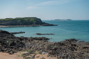 Saint-Malo sahilinin panoramik manzarası, altın kum, nazik dalgalar ve Brittany kıyısı boyunca tarihi cazibe.