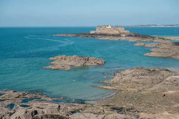 Saint-Malo sahilinin panoramik manzarası, altın kum, nazik dalgalar ve Brittany kıyısı boyunca tarihi cazibe.