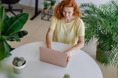 Genç bir kadın ev işlerinin rahatlığıyla uzaktan yakından ilgilenirken bilgisayarına odaklanmış..
