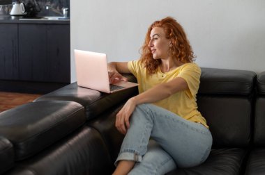 Genç bir kadın ev işlerinin rahatlığıyla uzaktan yakından ilgilenirken bilgisayarına odaklanmış..