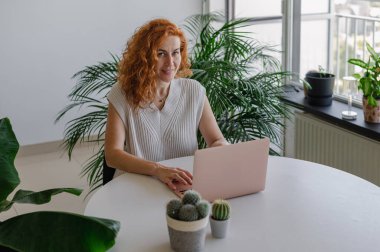 Genç bir kadın ev işlerinin rahatlığıyla uzaktan yakından ilgilenirken bilgisayarına odaklanmış..