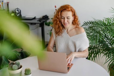 Genç bir kadın ev işlerinin rahatlığıyla uzaktan yakından ilgilenirken bilgisayarına odaklanmış..