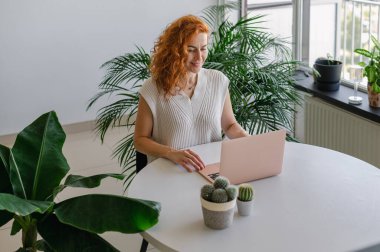 Genç bir kadın ev işlerinin rahatlığıyla uzaktan yakından ilgilenirken bilgisayarına odaklanmış..