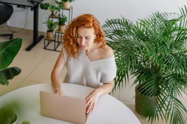 Genç bir kadın ev işlerinin rahatlığıyla uzaktan yakından ilgilenirken bilgisayarına odaklanmış..