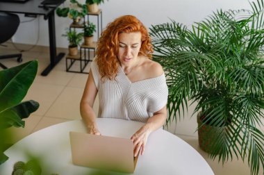 Genç bir kadın ev işlerinin rahatlığıyla uzaktan yakından ilgilenirken bilgisayarına odaklanmış..