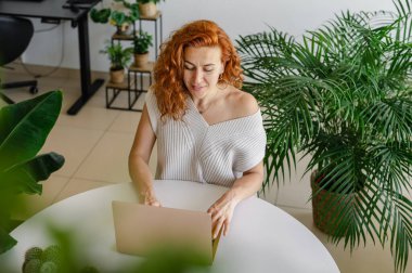 Genç bir kadın ev işlerinin rahatlığıyla uzaktan yakından ilgilenirken bilgisayarına odaklanmış..