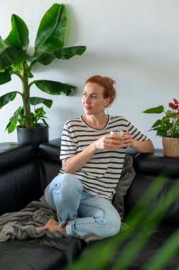 Hayalperest genç kadın, kanepede oturuyor ve sıcak bir fincan çayın tadını çıkarıyor..