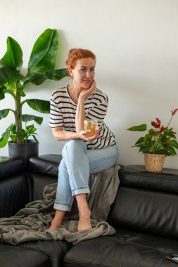 Hayalperest genç kadın, kanepede oturuyor ve sıcak bir fincan çayın tadını çıkarıyor..