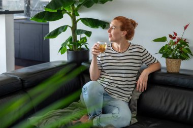 Hayalperest genç kadın, kanepede oturuyor ve sıcak bir fincan çayın tadını çıkarıyor..