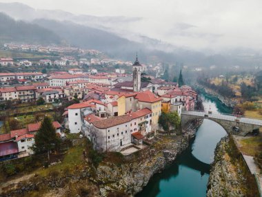 Slovenya 'daki Soca Nehri' nin turkuaz suları boyunca uzanan ve tarihi cazibesi ve doğal güzelliğiyle tanınan Kanal köyünün manzaralı manzarası.