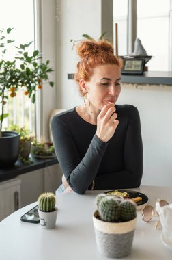 Çekici, olgun bir kadın sıcak mutfağında yemek yiyor. Günlük hayatın huzurlu anı..