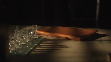 Akşamları masada kahverengi deri bir günlük. Doğal ışık ve arka planda satranç tahtası olan gölgeler.