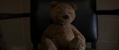 Bir oyuncak ayı loş bir odada bir sandalyeye oturtulur. Yalnızlık ve durgunluk hissi verir..