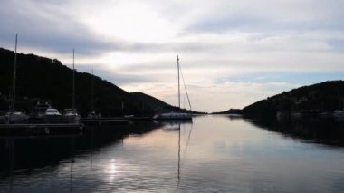 Yunanistan 'ın Lefkada adasındaki Sivota körfezinde gün doğumuna zum bulutlu gökyüzü ve altın ışığın durgun suya yansıması.