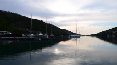 Yunanistan 'ın Lefkada adasındaki Sivota Körfezi' nde güneşin doğuşunun bir yansıması bulutlu bir gökyüzü ve sakin suya yansıyan altın ışıkla.