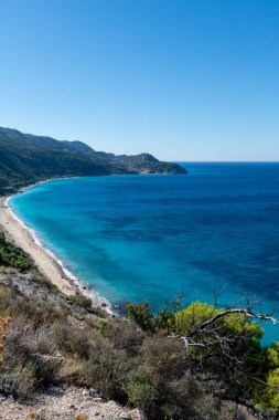 Derin mavi kristal berrak deniz ve bulutsuz mavi gökyüzü ile güzel, uzun bir sahil manzarası..