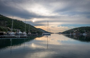 Sivota körfezinde gün doğumu, Lefkada adası, Yunanistan bulutlu gökyüzü ve durgun suya yansıyan altın ışıkla.