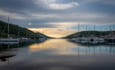 Sivota körfezinde gün doğumu, Lefkada adası, Yunanistan bulutlu gökyüzü ve durgun suya yansıyan altın ışıkla.