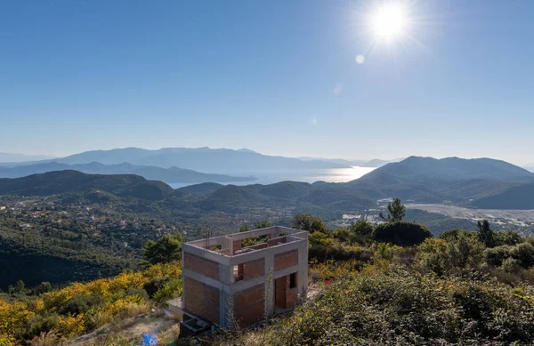 A house under construction on a mountain side with stunning panoramic view of the sea and landscape below.