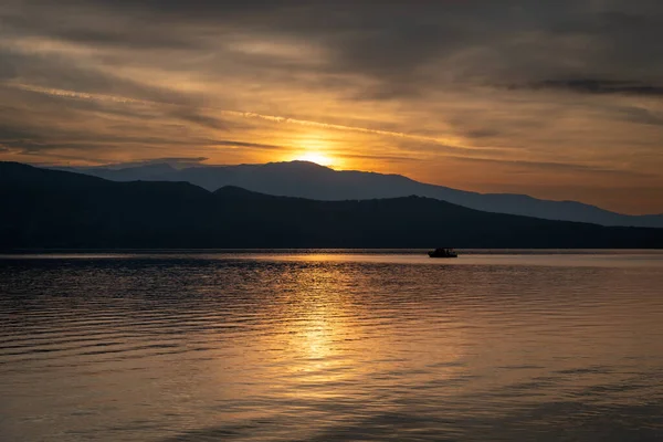 stock image A small fishing out at sea caught in the reflected light of the sun rising over the hill.