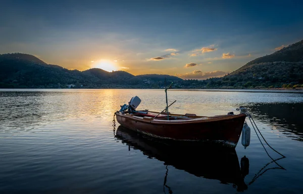 A old wooden boat on a sea bay with calm waters with the sun rising over the hill top.