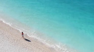 Güzel kumlu bir sahilde yürüyen bir turist yumuşak dalgalar ve berrak suyla.