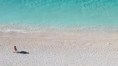 Güzel, ıssız bir kumsalda yürüyen bir turist. Yumuşak dalgaları ve berrak suları olan..