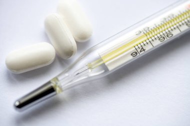 Beyaz arkaplanda izole edilmiş bazı ilaç haplarıyla analog termometreyi kapat.