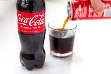 London. UK- 01.29.2023. A bottle of Coca Cola original taste isolated in white with a person pouring a can of the drink into a glass.