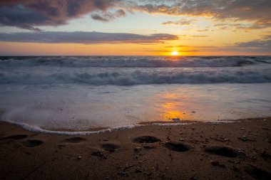 Gün batımında kumlu zemine vuran ayak izleri ve dalgalar..