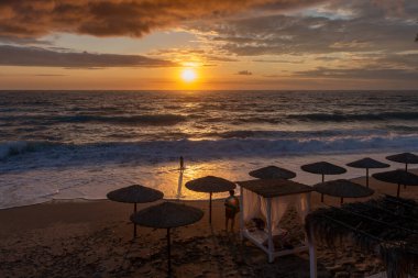 Tatilcilerin deniz ve muhteşem gün batımı manzarasının tadını çıkardığı kumlu bir sahil..