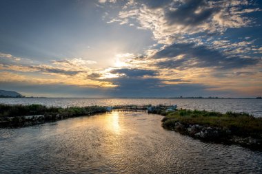 Gün batımında bir balık çiftliği. Güneş bulutları aydınlatıyor ve suya ışık tutuyor..