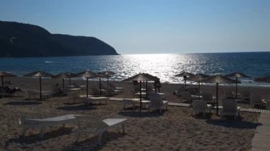 Lefkada adası. Yunanistan - 06.21.2023. Agios Ioannis plajı manzarası. Sahilde güneş ışığı alan turistler ve suda uçurtma sörfçüleri..