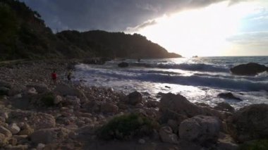 Lefkada adası. Yunanistan - 06.17.2023. Kıyı şeridini keşfeden ve güçlü dalgalarla oynayan turistler.
