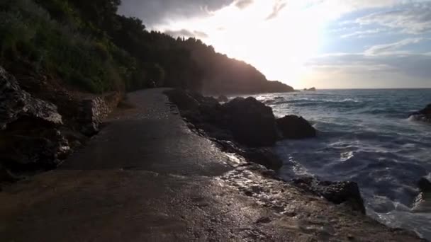 波が強く 丘の後ろに太陽が沈む海のそばを歩くツアー — ストック動画