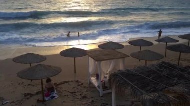 Lefkada adası. Yunanistan - 06.17.2023. Turistler güzel kumlu bir plajda gün batımının tadını çıkarıyorlar..