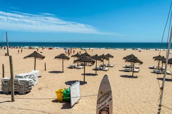 Stock image Lisbon. Portugal- 07.08.2023. Surf board, sun beds and umbrellas at Carcavelos Beach with beach sports in the background.