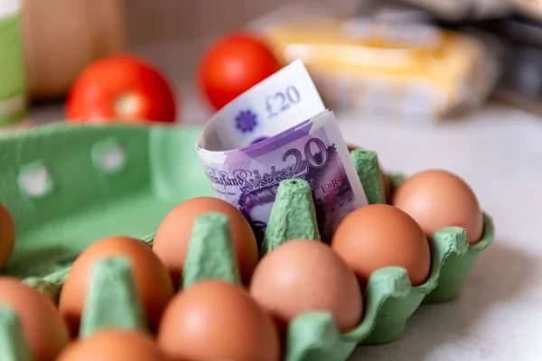 A cost of living, food inflation concept with Pound Sterling bank notes in a packet of eggs.